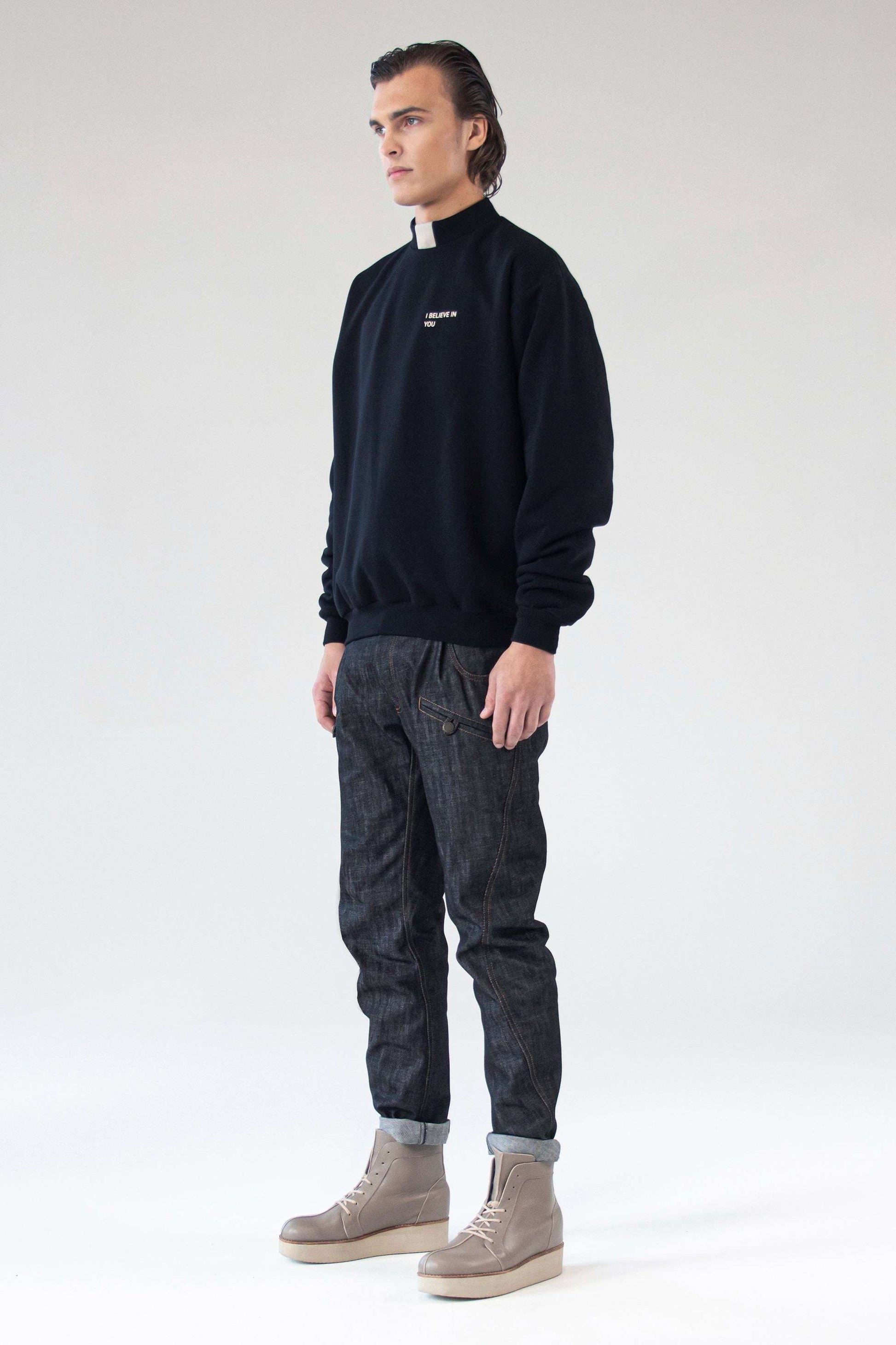 Close-up portrait of model wearing black One Wolf sweater with subtle ‘I Believe In You’ silk print.